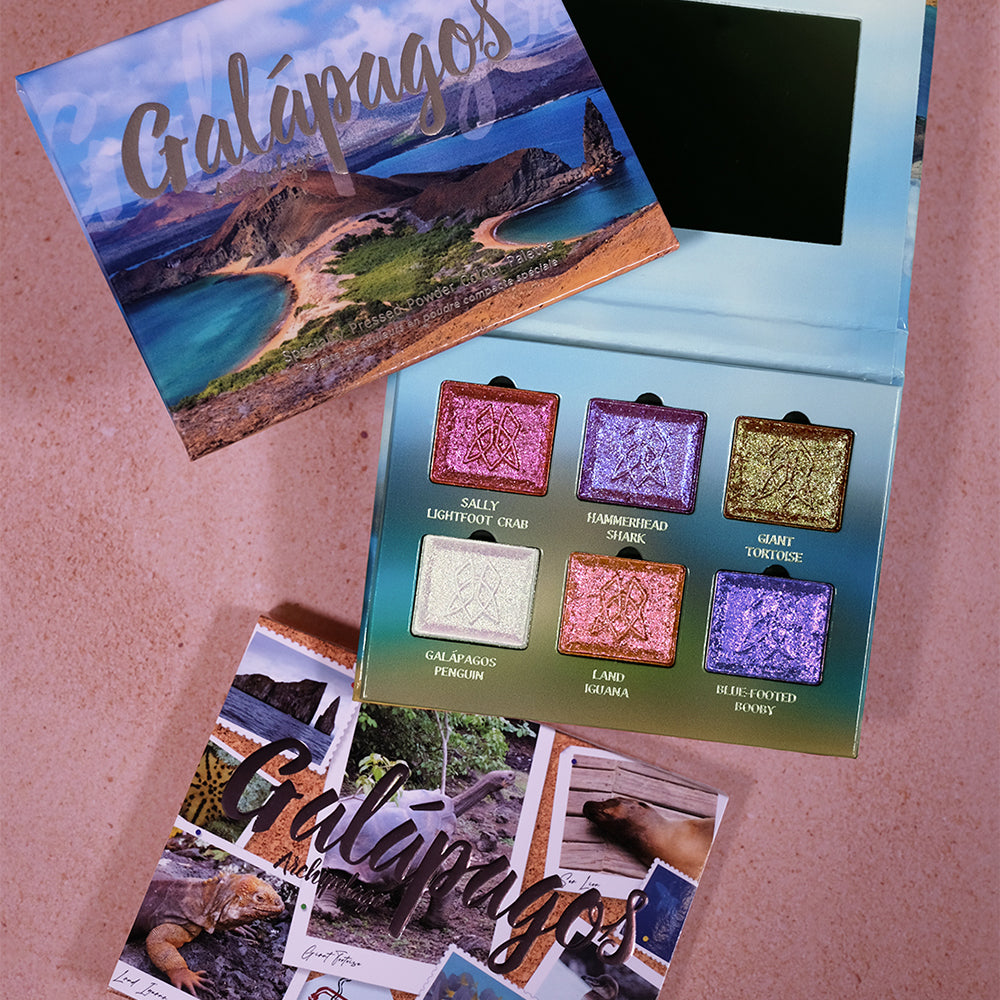 Galápagos Palette displayed on a pink textured surface, featuring the artistic packaging and an open palette with six shimmering shadow pans.